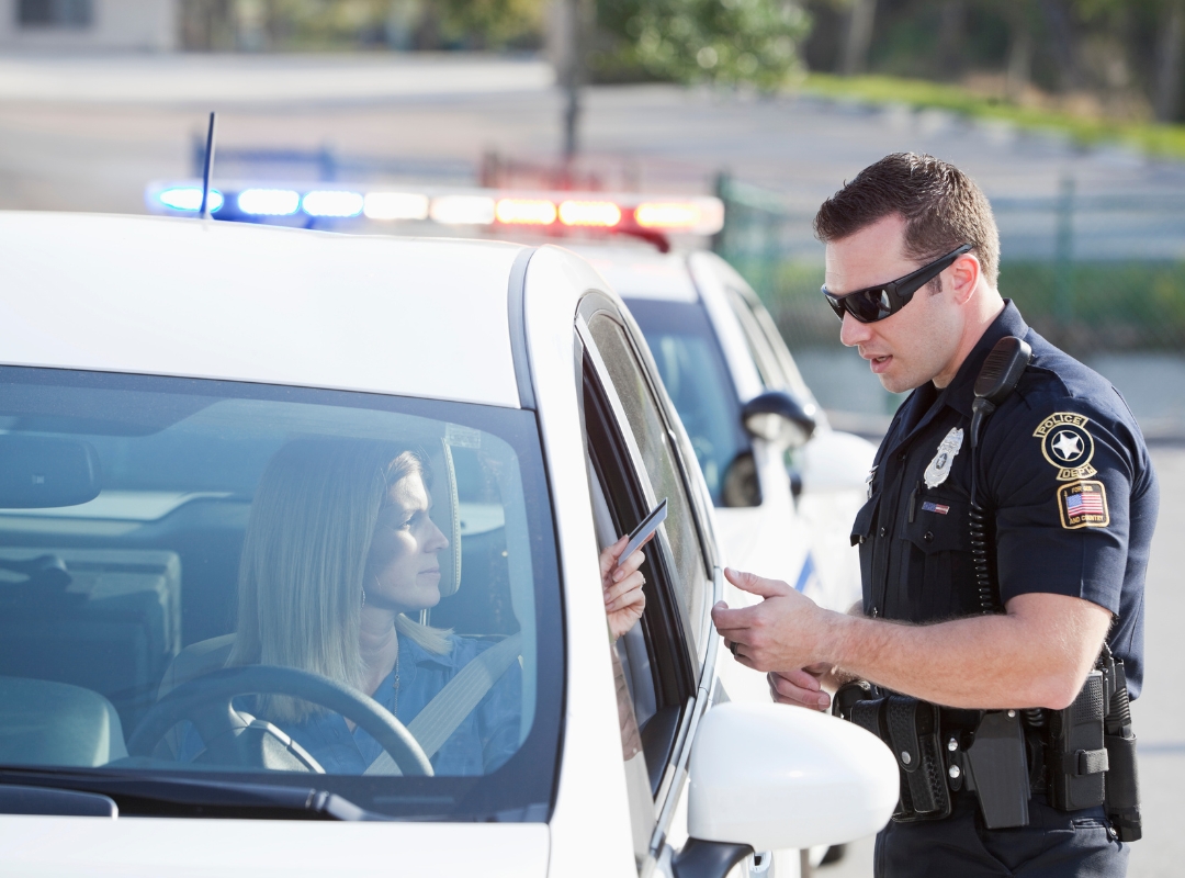 Women in car handing driver's license to a police officer.